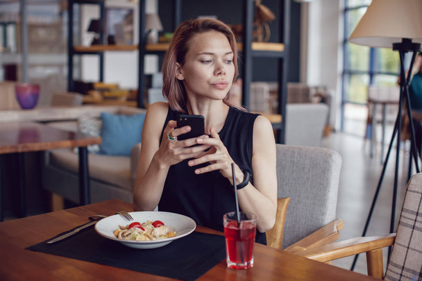 Femme attrayante utilisant smartphone et manger dans un café
. - Photo, image