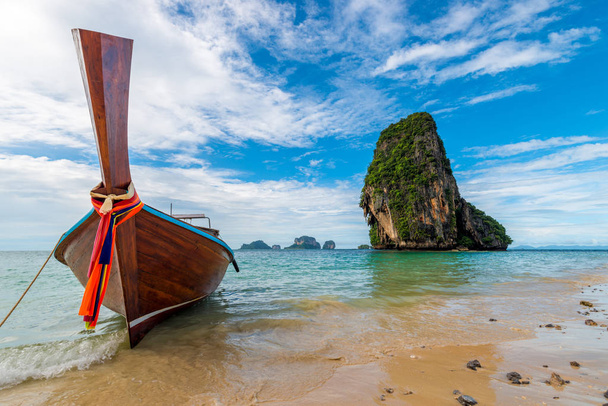Деревянная тайская лодка с мотором на фоне высокой скалы
 - Фото, изображение