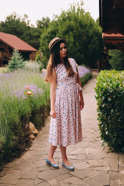Young beautiful woman in long dress and stylish hat enjoys good weather in her country house  - Foto, imagen