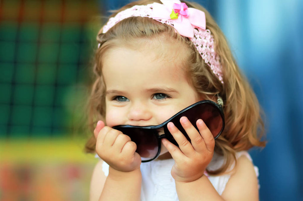 süßes einjähriges Mädchen, das Mamas Sonnenbrille gestohlen hat und glücklich ist, sie zu tragen, um wie ein Erwachsener auszusehen - Foto, Bild
