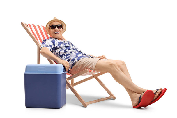 man sitting in a deck chair next to a cooling box - Foto, afbeelding