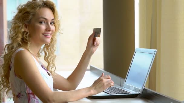 Piękna kobieta, trzymając w ręku karty kredytowej i wprowadzenie kodu zabezpieczającego przy użyciu klawiatury laptopa - Materiał filmowy, wideo