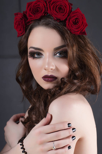 красивая молодая женщина с цветами роз в волосах. красотка с макияжем на темном фоне. темно-красные помады крупным планом
 - Фото, изображение