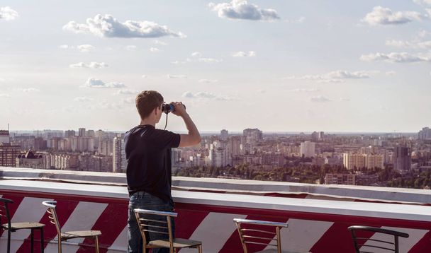 Jeune homme regardant à travers des jumelles sur le toit d'un bâtiment
 - Photo, image