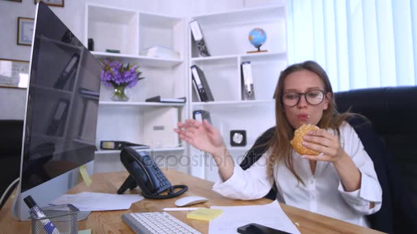 Busy woman talking on the phone while having burger - Filmati, video