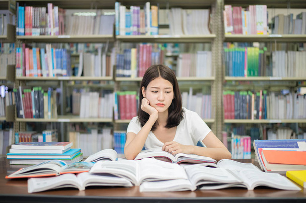 Asian woman student boring reading book at library with a lot of - Фото, изображение