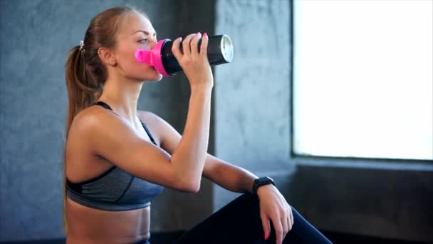 Beautiful girl in sport clothes drinking water after workout in the gym. - Video, Çekim