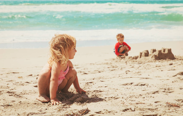 little girl and boy play with sand on beach - Fotó, kép