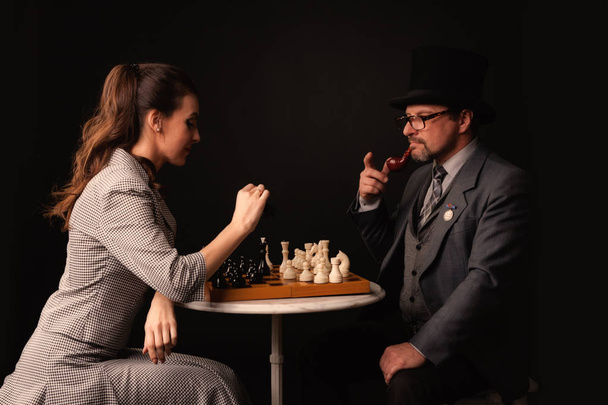A man with a girl plays chess and smokes a pipe on a dark backgr - Foto, immagini