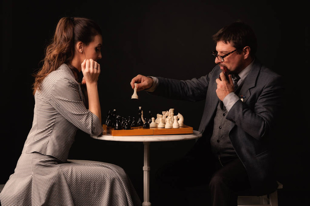A man with a girl plays chess and smokes a pipe on a dark backgr - Zdjęcie, obraz