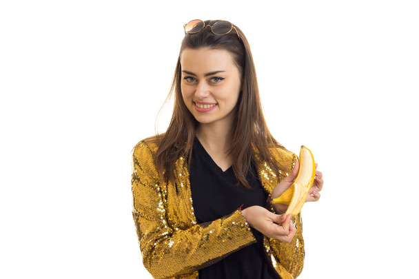 Cheerful stylish girl in golden jacket with banana smiling on camera - Valokuva, kuva
