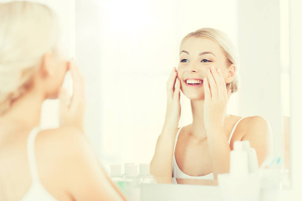 happy woman applying cream to face at bathroom - Zdjęcie, obraz