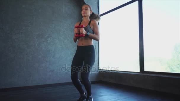 Спортивна жінка займається сидінням і стрибками, вона тримає гантелі
 - Кадри, відео