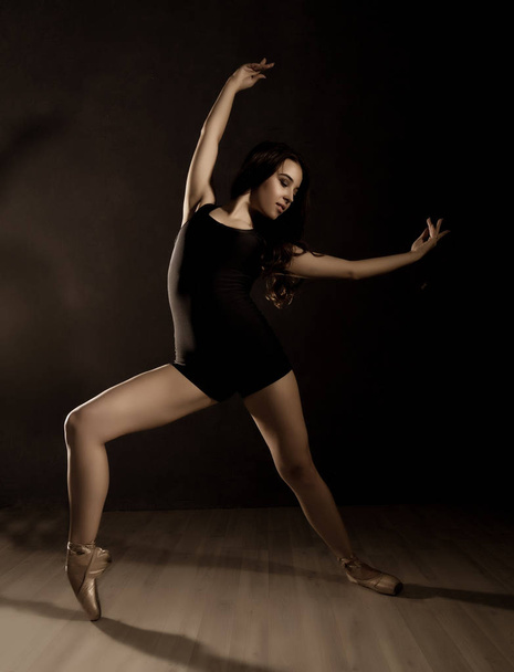 young beautiful ballet dancer in pointe shoes, dancing in a dark background - Foto, imagen