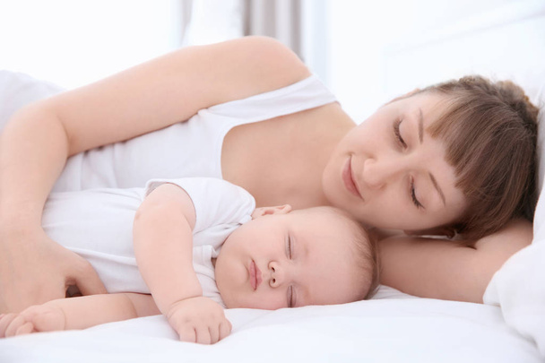 Jonge vrouw met schattige slapende baby liggend op bed thuis - Foto, afbeelding