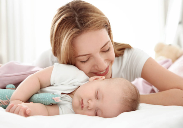 Young woman with cute sleeping baby lying on bed at home - Valokuva, kuva