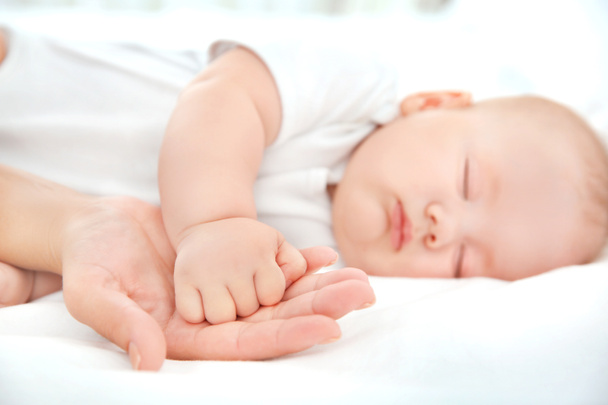 Young woman holding hand of cute sleeping baby, closeup - Foto, immagini