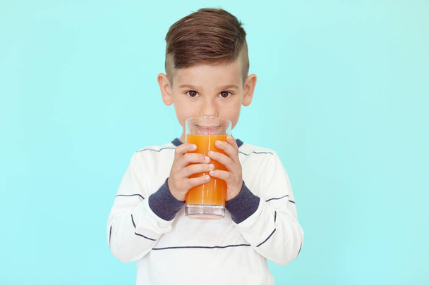 Cute little boy drinking juice on color background - Photo, image