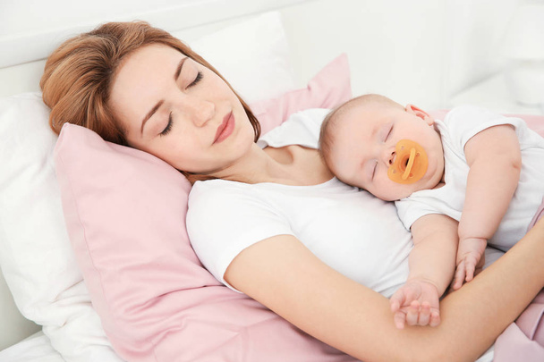 Young woman with cute baby sleeping on bed at home - Фото, изображение
