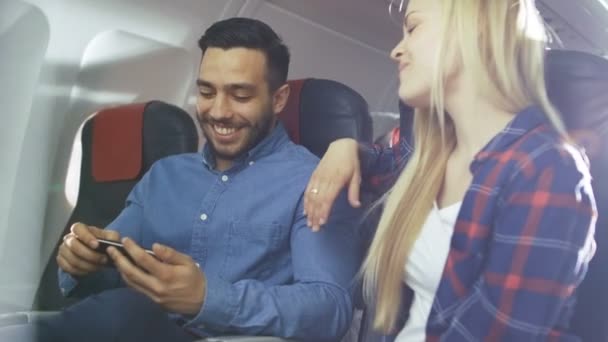 Szép fiatal szőke szép Spanyol férfi játszani Holiday járatuk a Smartphone. Új kereskedelmi repülőgép belseje látható. - Felvétel, videó