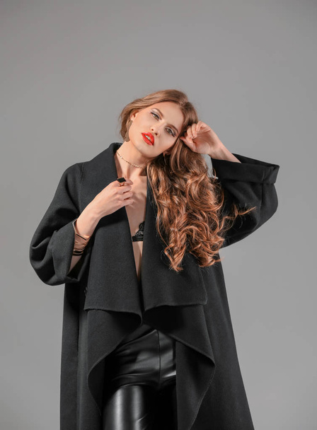 Beautiful stylish woman in dark coat on grey background - Фото, зображення