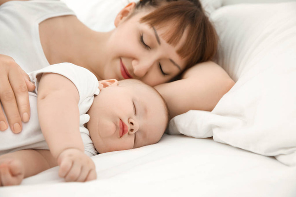 Молодая женщина с симпатичным спящим ребенком лежит на кровати дома
 - Фото, изображение