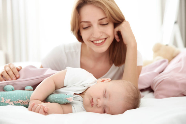 Young woman with cute sleeping baby lying on bed at home - Фото, зображення