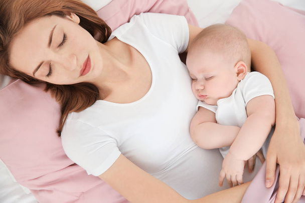 Young woman with cute baby sleeping on bed at home - Foto, immagini