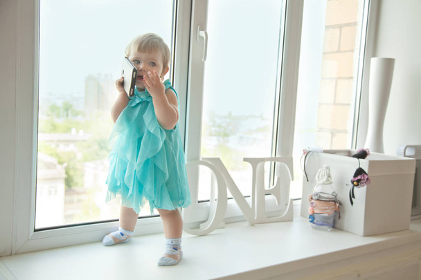 κοριτσάκι ενός έτους που μιλάμε από το τηλέφωνο κοντά στο παράθυρο - Φωτογραφία, εικόνα