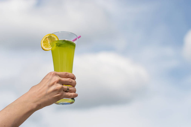 Woman holding a glass of homemade cold lemonade with fresh lemon slice and mint - Fotoğraf, Görsel