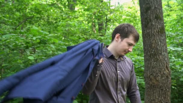молодий чоловік стоїть в лісі, кидає куртку на плече і робить селфі. повільний рух
 - Кадри, відео