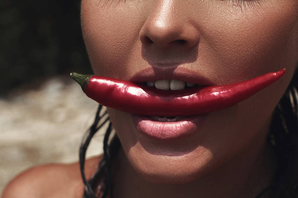 Női száj tartja a red hot chili paprika. Ő már élénkvörös rúzs ajkán. - Fotó, kép