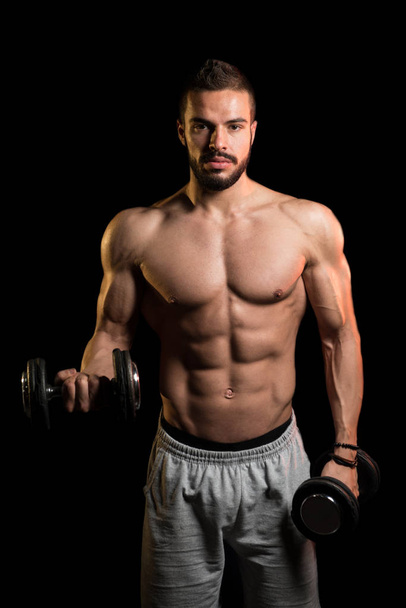 Model Exercising Biceps With Dumbbells On Black Background - Фото, изображение
