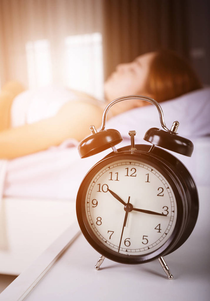 ρολόι δείξει 10 π.μ. και η γυναίκα στον ύπνο στο κρεβάτι με το ηλιακό φως σε mor - Φωτογραφία, εικόνα