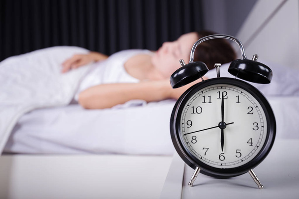 ρολόι δείξει 6 η ώρα και η γυναίκα στον ύπνο στο κρεβάτι  - Φωτογραφία, εικόνα