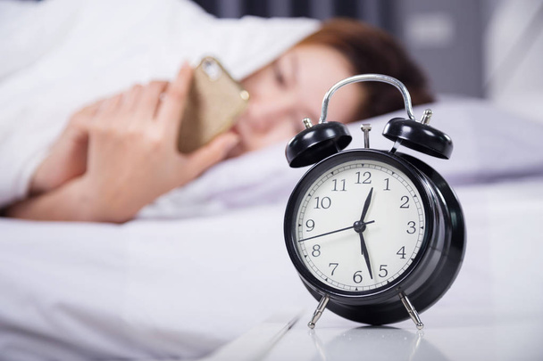 zegar z kobieta za pomocą jej smartphone na łóżku - Zdjęcie, obraz