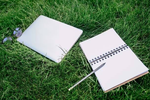 Notebook en digitaal apparaat op gras  - Foto, afbeelding