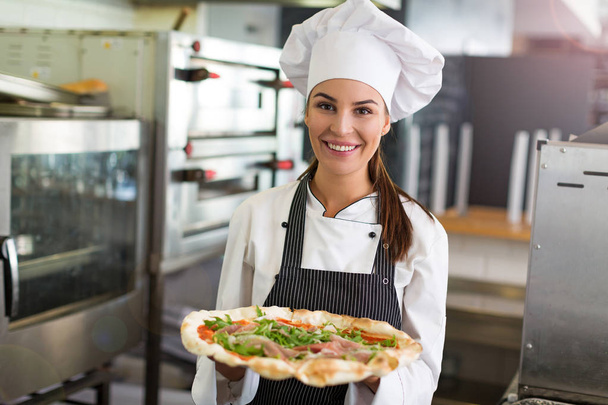 Smiling chef holding fresh pizza in kitchen - Foto, Imagen