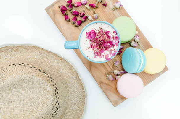 Morning fresh and tasty macarons, cappuccino and roses petal with straw hat on table - Photo, Image