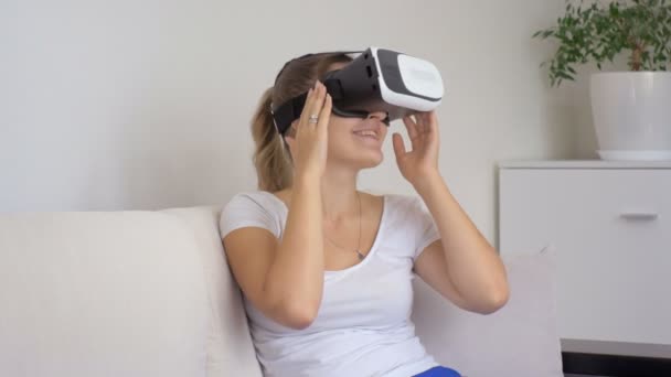 Portrait of young smiling woman sitting on sofa and using virtual reality headset and watching 3d movie. Footage shot at 4k - Footage, Video