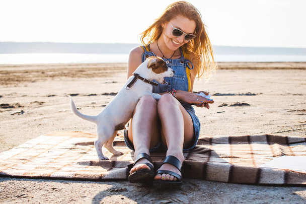 Young stylish hipster girl playing dog puppy jack russell on the beach - Valokuva, kuva