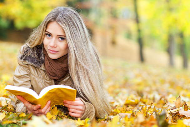 Pretty young woman reading in a park in autumn - Photo, Image