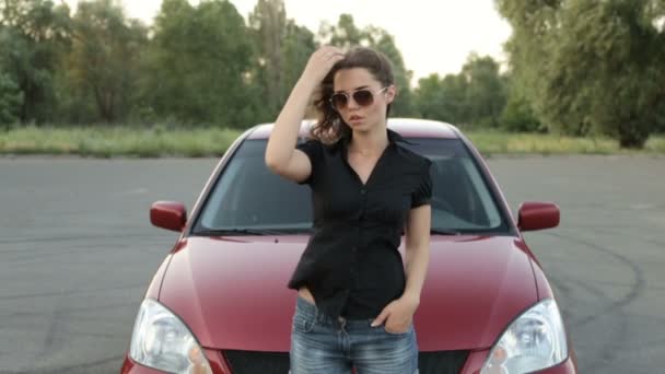 Dívka v sluneční brýle představují pozadí červené auto - Záběry, video
