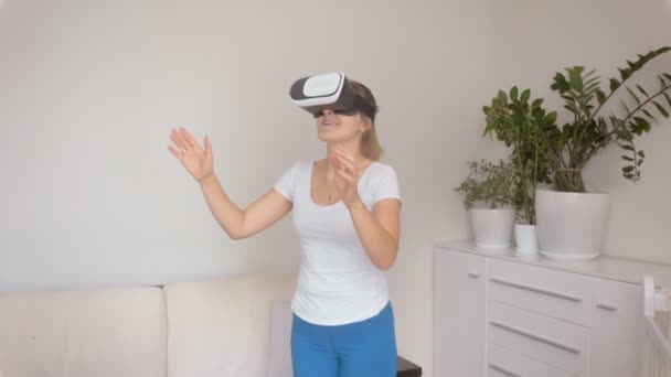Mujer joven asombrada con auriculares VR caminando por la habitación y atrapando objetos delante de ella. Filmación a 4k
 - Metraje, vídeo