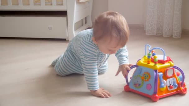 Lindo niño de 1 año de edad en pijama arrastrándose en el suelo y jugando con el juguete
 - Metraje, vídeo