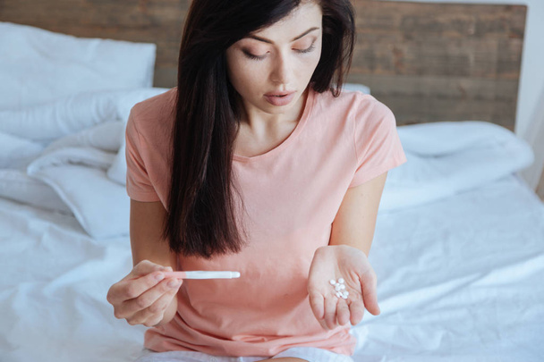 Pregnant brunette looking distressingly at pills - Photo, Image
