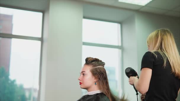 Η ξανθιά κομμωτήριο ισιώνει τα βρεγμένα μαλλιά με πιστολάκι για τα μαλλιά και χτένα - Πλάνα, βίντεο