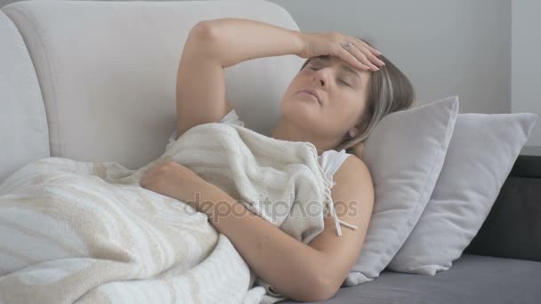 Nieszczęśliwa kobieta młody cierpiących na ból głowy leżącej kanapie w salonie. Nagrania w rozdzielczości 4k - Materiał filmowy, wideo