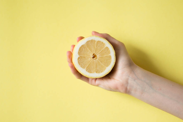 Lemon in woman's hand on a yellow background - Foto, imagen