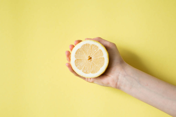 Lemon in woman's hand on a yellow background - Zdjęcie, obraz